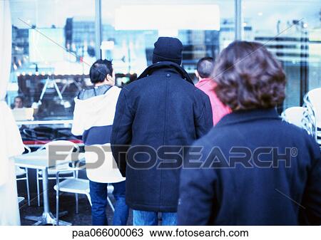 Stock Image - Group of young people outside cafe, rear view. Fotosearch