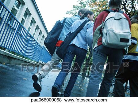 Stock Photo - Group of young people walking down sidewalk with backpacks, low angle, rear view. Fotosearch