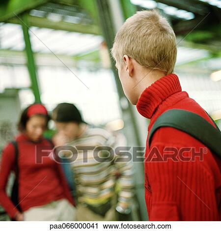 Stock Image - Teenage boy looking at two teenage girls, blurred in background, on subway platform. Fotosearch