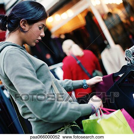 Teenage girl looking at rack of clothes, holding shopping bags, outdoors View Large Photo Image Stock Image - Teenage girl looking at rack of clothes, holding shopping bags, outdoors. Fotosearch