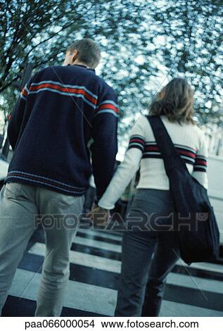 Young couple holding hands crossing on pedestrian crossing, rear view View Large Photo Image Picture - Young couple holding hands crossing on pedestrian crossing, rear view. Fotosearch
