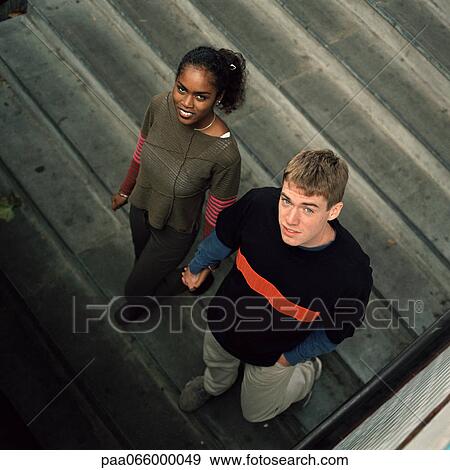 Young couple walking downstairs, looking up at camera, high angle view View Large Photo Image Stock Photo - Young couple walking downstairs, looking up at camera, high angle view. Fotosearch
