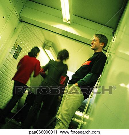 Stock Image - Young man standing in subway corridor, side view, people walking, rear view in background. Fotosearch