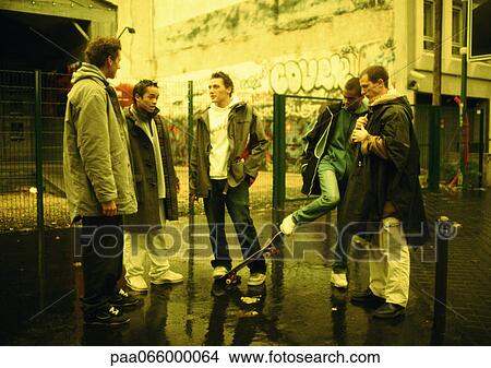 Young men hanging out together on street corner, wall with grafitti in background View Large Photo Image Picture - Young men hanging out together on street corner, wall with grafitti in background. Fotosearch