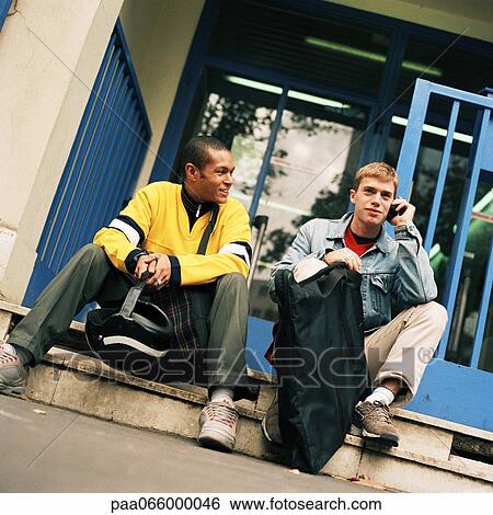 Young men sitting on steps with backpacks, one using cell phone. View Large Photo Image Stock Photograph - Young men sitting on steps with backpacks, one using cell phone.. Fotosearch