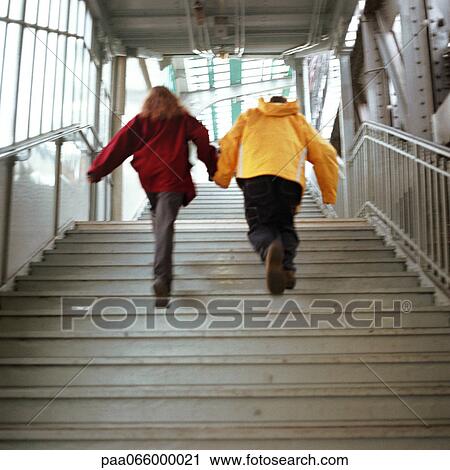 Stock Image - Young people holding hands and walking up stairs in elevated subway station. Fotosearch