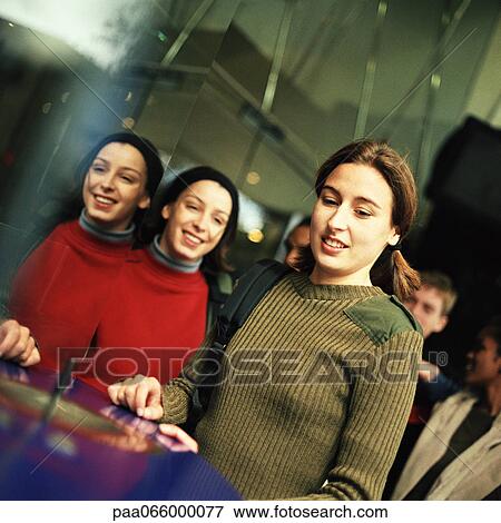 Stock Photo - Young people inside, one young woman reflected in mirror. Fotosearch
