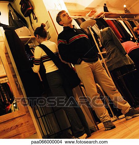 Young woman looking at clothes in clothing store, and young man standing with hands in pockets View Large Photo Image Picture - Young woman looking at clothes in clothing store, and young man standing with hands in pockets. Fotosearch