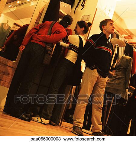 Stock Photo - Young women looking at clothes in store, young man standing with back to them. Fotosearch