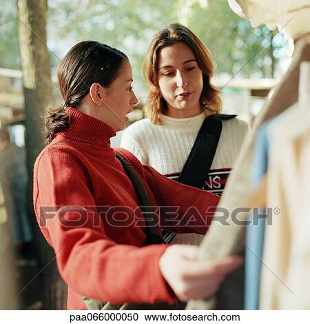 Stock Image - Young women looking at clothing on rack, outdoors. Fotosearch