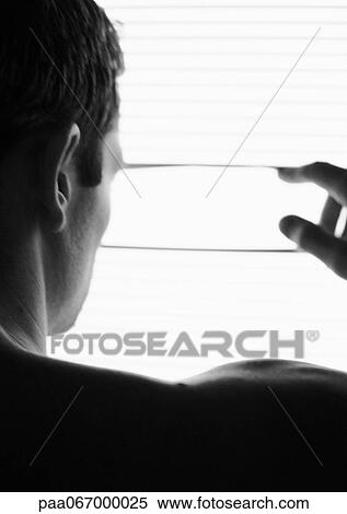 Stock Photography - Man looking through blinds, rear view, head and shoulders, partial view, black and white.. Fotosearch