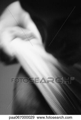 Stock Photo - Man pulling shirt off, head in shadow in foreground, blurred, close-up, black and white.. Fotosearch