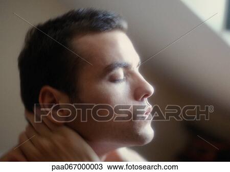 Stock Image - Man sitting with hands around neck and eyes closed, close-up, side view . Fotosearch