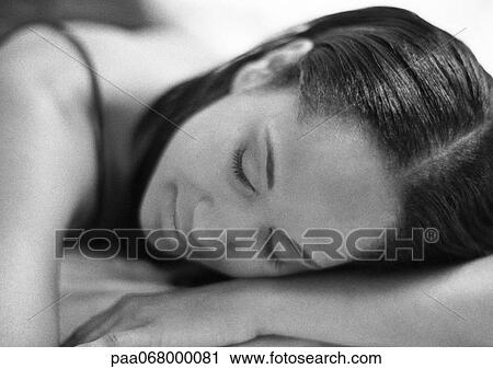 Stock Image - Woman lying with head on arm and eyes closed, close-up, black and white.. Fotosearch