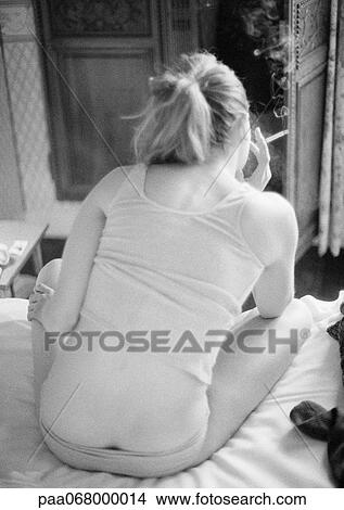 Picture - Woman sitting on bed smoking, rear view, black and white.. Fotosearch