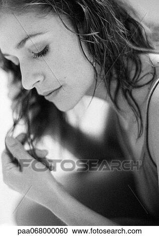 Stock Image - Woman with eyes lowered touching hair, close-up, black and white.. Fotosearch