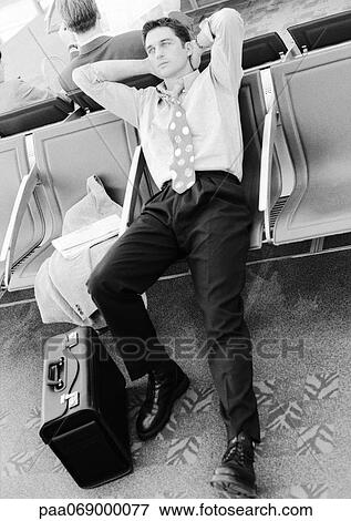 Stock Photo - Businessman in airport lounge leaning back in seat, black and white.. Fotosearch