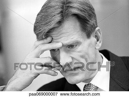 Stock Photo - Businessman leaning head forward, holding face with fingers, close-up, black and white.. Fotosearch