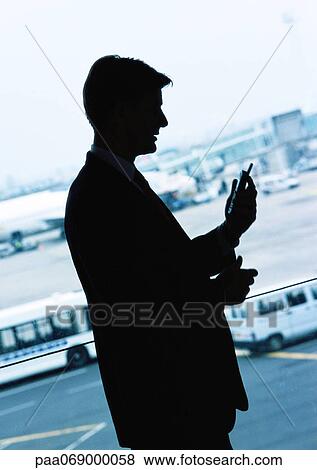 Businessman looking at cellular phone in airport, silhouette. View Large Photo Image Stock Photo - Businessman looking at cellular phone in airport, silhouette.. Fotosearch