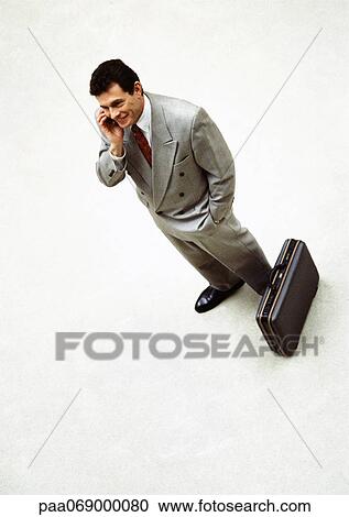Businessman talking on cellular phone standing next to briefcase, high angle view View Large Photo Image Stock Image - Businessman talking on cellular phone standing next to briefcase, high angle view. Fotosearch