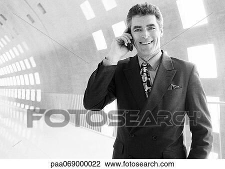 Businessman using cellular phone in corridor, smiling at camera, black and white View Large Photo Image Stock Image - Businessman using cellular phone in corridor, smiling at camera, black and white. Fotosearch