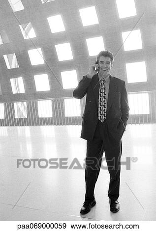 Stock Photo - Businessman using cellular phone in corridor, full length, b&w. Fotosearch