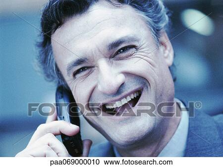 Stock Image - Businessman using cellular phone, laughing, close-up, cool toned.. Fotosearch