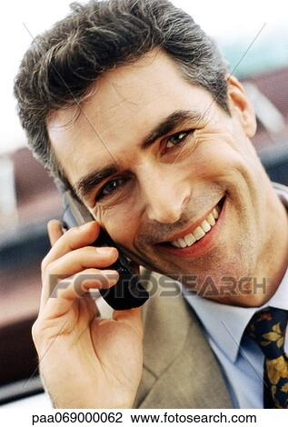 Stock Image - Businessman using cellular phone, smiling at camera, close-up, portrait.. Fotosearch