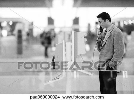 Businessman using pay phone in terminal, black and white. View Large Photo Image Picture - Businessman using pay phone in terminal, black and white.. Fotosearch