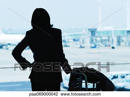 Stock Image - Businesswoman next to luggage, silhouette, airplanes in background. Fotosearch