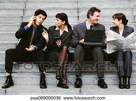 Stock Photograph - Four business people sitting on steps, interacting.. Fotosearch