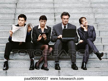 Stock Photo - Four business people wearing suits, sitting on steps, reading newspaper. Fotosearch