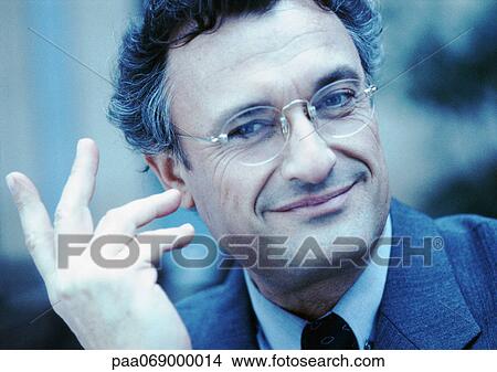 Man wearing suit and glasses, smiling at camera, hand in air, close-up, cool toned. View Large Photo Image Picture - Man wearing suit and glasses, smiling at camera, hand in air, close-up, cool toned.. Fotosearch