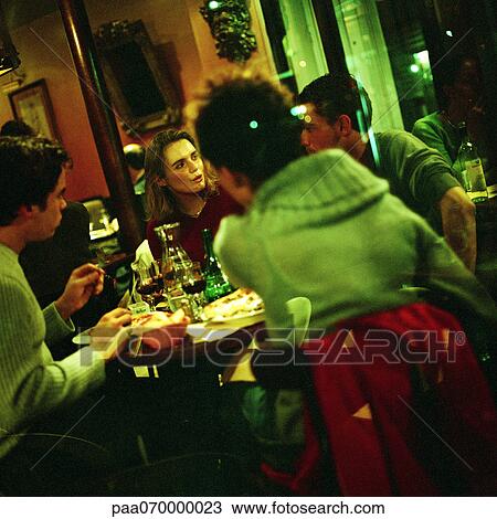 Stock Image - Group of young people eating in restaurant. Fotosearch