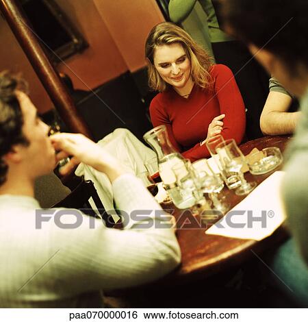 Stock Photograph - Group of young people sitting at table, drinking. Fotosearch