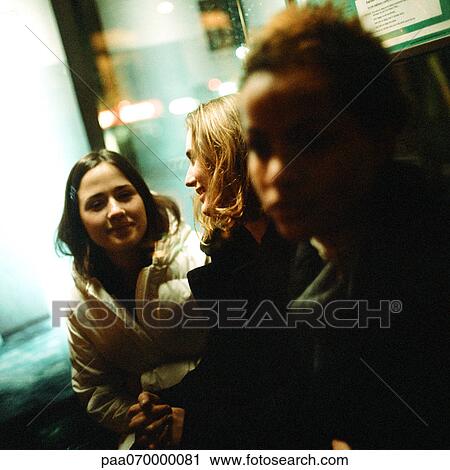 Stock Image - Three young women sitting in bus shelter at night, close-up. Fotosearch