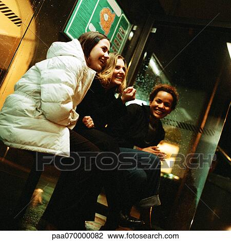 Three young women sitting in bus shelter at night, laughing View Large Photo Image Stock Image - Three young women sitting in bus shelter at night, laughing. Fotosearch