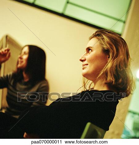 Two young women sitting, one smoking View Large Photo Image Stock Image - Two young women sitting, one smoking. Fotosearch