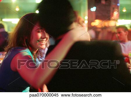 Stock Photography - Young man and woman talking in bar, woman with hand around man's neck. Fotosearch