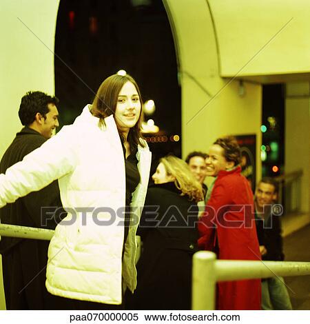 Young woman in coat smiling at camera, group of young people in background View Large Photo Image Stock Photography - Young woman in coat smiling at camera, group of young people in background. Fotosearch