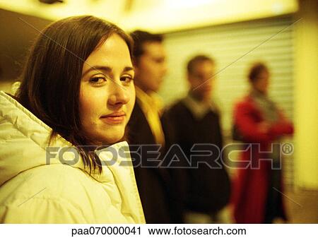 Stock Image - Young woman looking at camera, young people standing in background. Fotosearch