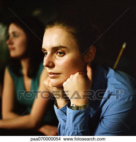 Picture - Young woman resting head on hands, portrait, second young woman sitting in background. Fotosearch