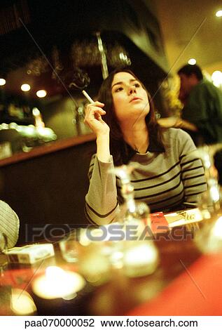 Stock Image - Young woman sitting in cafe, smoking a cigarette.. Fotosearch