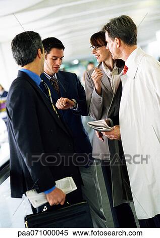 Business people standing together, one looking down at watch View Large Photo Image Stock Photography - Business people standing together, one looking down at watch. Fotosearch