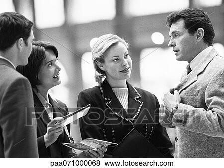 Stock Photo - Business people talking, one holding ticket, b&w.. Fotosearch