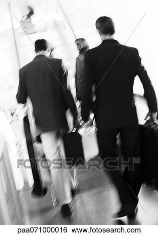 Stock Photograph - Business people walking to escalator, rear view, blurred, b&w.. Fotosearch