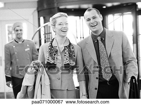 Businessman and businesswoman in hotel in front of bellhop, smiling at camera, b&w. View Large Photo Image Stock Photo - Businessman and businesswoman in hotel in front of bellhop, smiling at camera, b&w.. Fotosearch