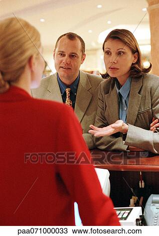 Stock Image - Businessman and businesswoman talking to receptionist.. Fotosearch