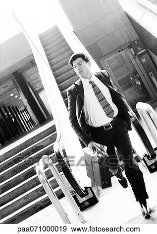 Stock Photo - Businessman getting off escalator, running and holding briefcase, blurred, b&w.. Fotosearch