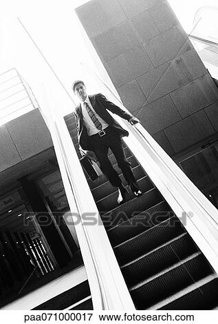Stock Photo - Businessman going down escalator, b&w.. Fotosearch